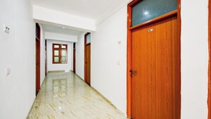 A hallway with a marble floor, wooden doors, and a window with multiple panes. - Anandam Grand (New Delhi)