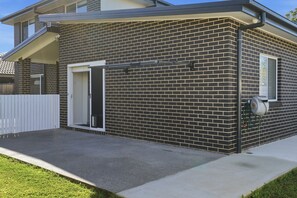 Ein zweigeschossiges Backsteinhaus mit überdachter Terrasse, einer weißen Tür und einem sichtbaren Gartenschlauch.