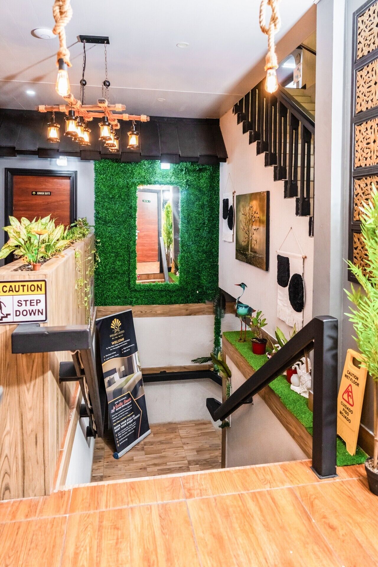 Ein Hotel-Empfangsbereich mit einem Holztresen, einem Warnschild, einem Willkommensschild und einer Treppe mit grüner Wand und Holzgeländer.