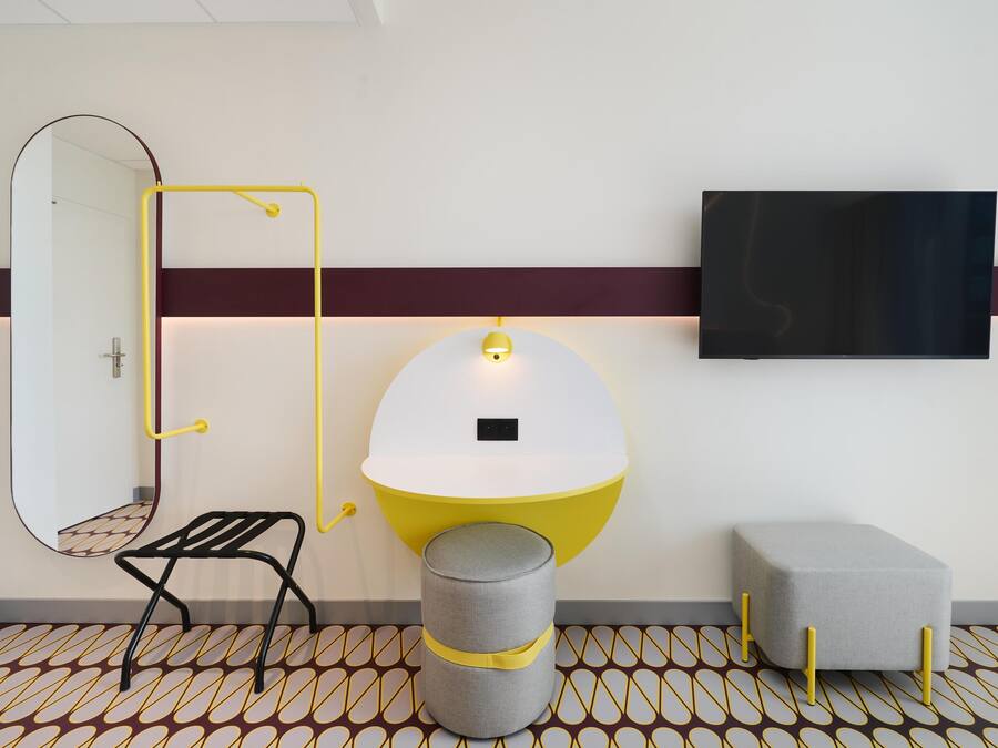 A modern bathroom with a mirror, a yellow and white sink, a grey stool, and a small ottoman.