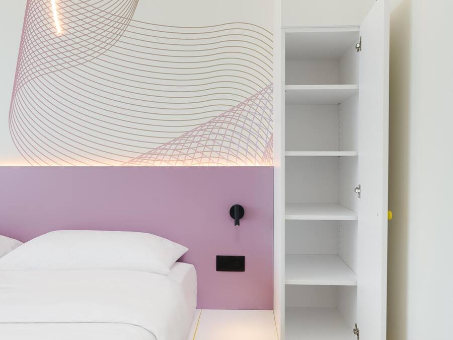 Um quarto moderno com uma cama branca, uma parede de destaque rosa e um chão com padrão geométrico.