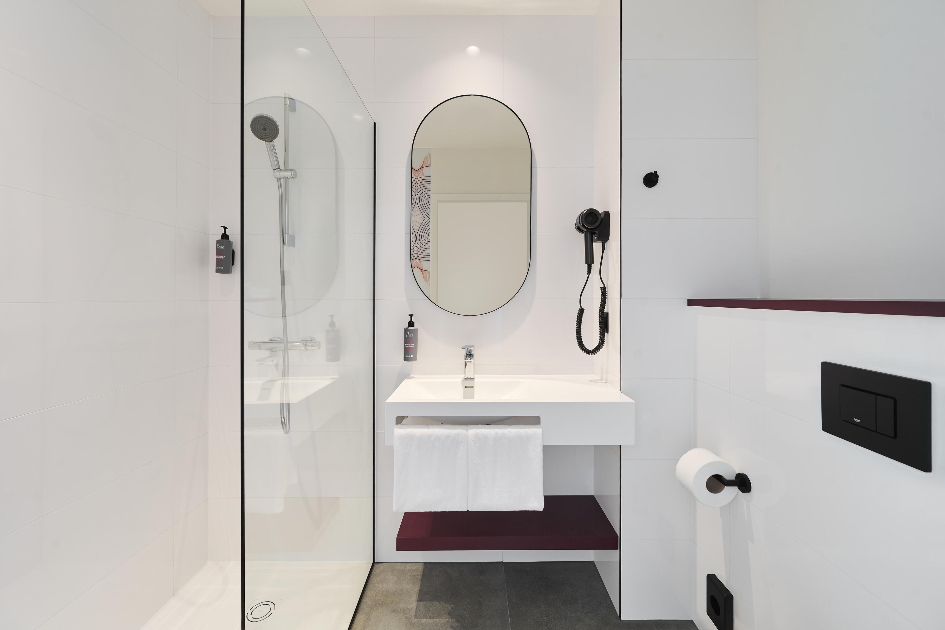 A modern bathroom with a glass shower enclosure, a white sink with a mirror, and a red towel rack.