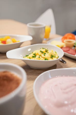 A breakfast table with various dishes including scrambled eggs, a pink dessert, and a cup of coffee.