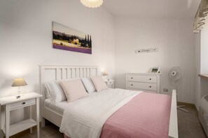 A bedroom with a bed, bedside tables, a nightstand, a wall-mounted artwork, a bedside lamp, a white dresser, and a floor fan. - Villa Vinea (100691-K1) - Momjan (Momjan)