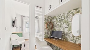 Quarto moderno com escrivaninha de madeira, cadeiras brancas, televisão de tela plana e parede com papel de parede tropical.
