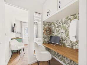 Ein modernes Zimmer mit Schreibtisch aus Holz, weißen Stühlen, einem Flachbildfernseher und einer Wand mit tropischem Wandpapier.