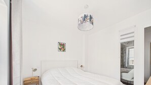 Quarto com cama, mesa de cabeceira, luminária, quadro na parede e janela com vista.
