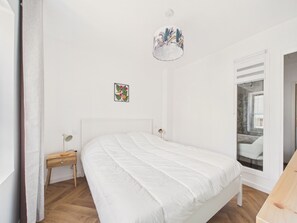 Ein Schlafzimmer mit einem Bett, einem Nachttisch, einer Lampe, einem Wandbild und einem Fenster mit Blick.