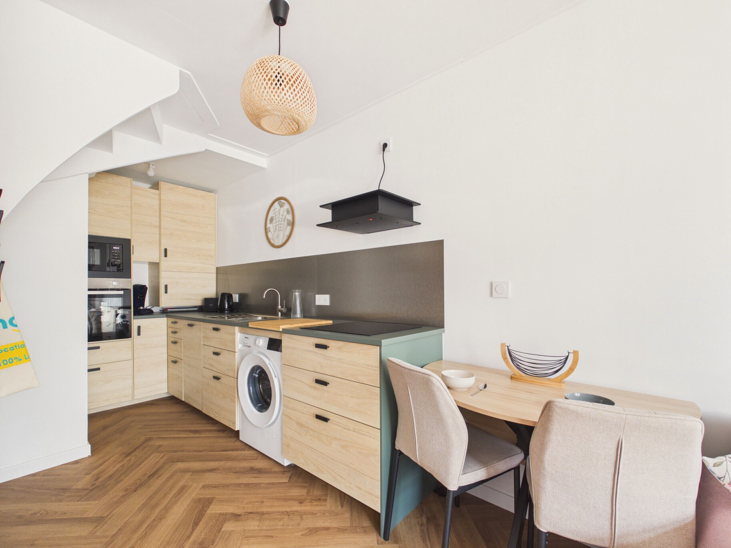 A modern kitchen with wooden cabinets, a built-in oven, a washing machine, and a dining area with a table and chairs.