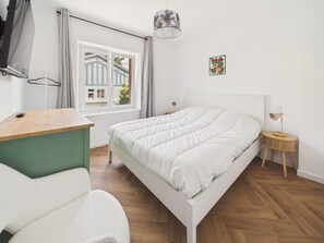 A bedroom with a bed, a desk, a chair, a bedside table, a lamp, a window with curtains, and a wall-mounted picture. - Stay for 2, walk everywhere, beach 500m (Dinard)