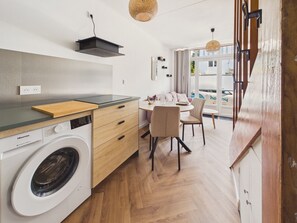 Eine kleine Küche mit Waschmaschine, Holz Arbeitsplatte und einem Essbereich mit Stühlen und Tisch.