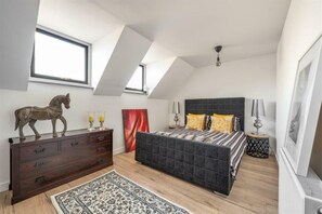 A bedroom with a dark headboard, a wooden dresser, a patterned rug, and a window with a view. - Contemporary 3BDR House in South Woodford (Greater London)