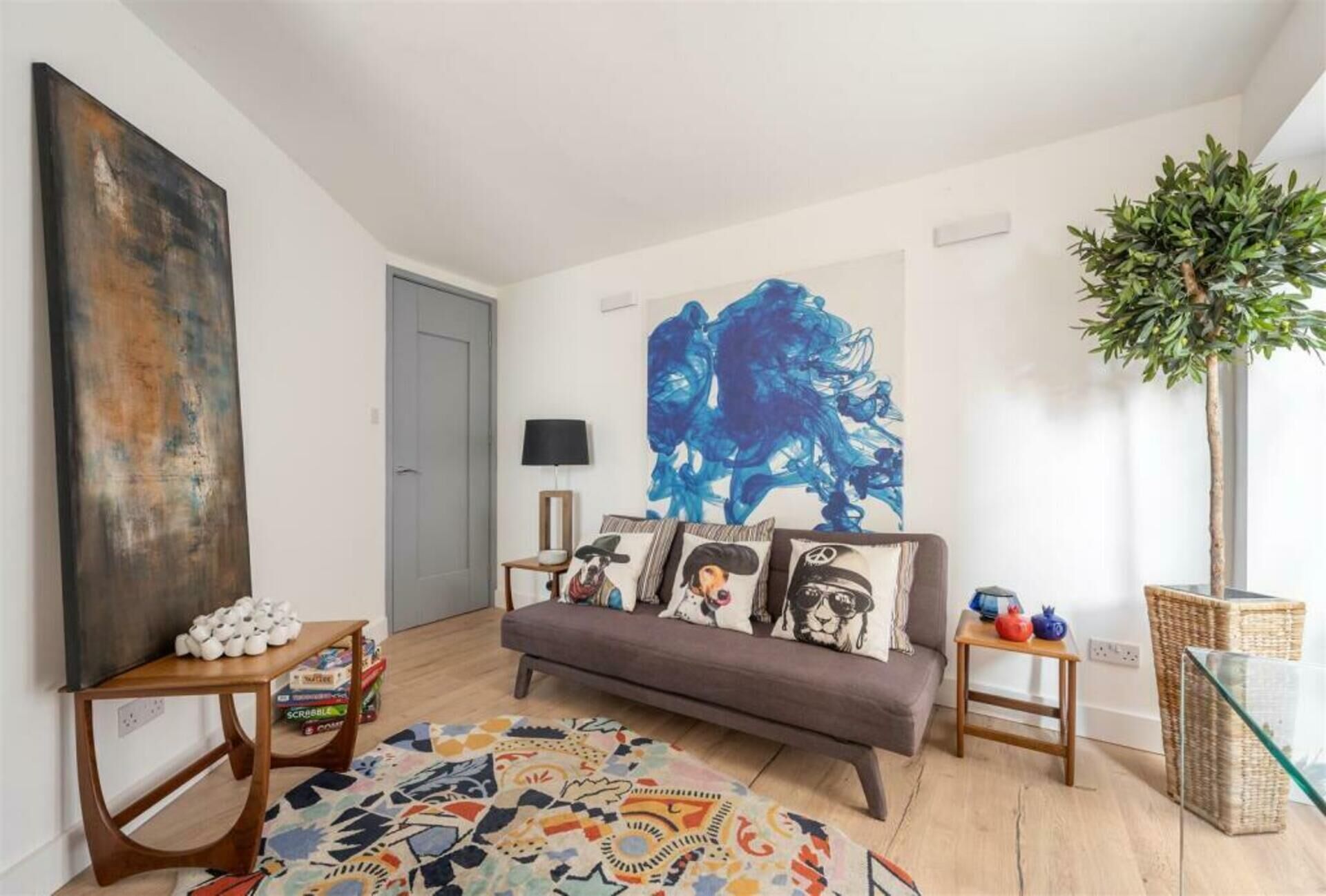 Een woonkamer met een bank, een salontafel, een vloerkleed, een schilderij en een plant.