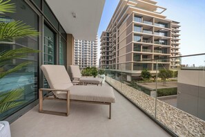 A balcony with a lounge chair, potted plants, and a view of a high-rise building. - StayShort - Stunning 2-Bedroom Apartment in Mina Rashid That Sleeps 6! (Dubai)