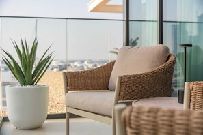 A wicker chair with a cushion, a potted plant, and a modern lamp on a balcony with a city view. - StayShort - Stunning 2-Bedroom Apartment in Mina Rashid That Sleeps 6! (Dubai)