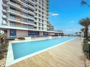 A modern hotel with a long swimming pool, a covered outdoor area, and a view of the sea. - StayShort - Stunning 2-Bedroom Apartment in Mina Rashid That Sleeps 6! (Dubai)