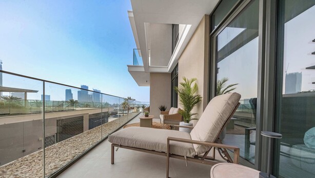 A balcony with a lounge chair, a small table, and a potted plant. - StayShort - Stunning 2-Bedroom Apartment in Mina Rashid That Sleeps 6! (Dubai)