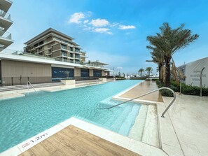 A swimming pool with a 1.2m depth marker, adjacent to a modern building with balconies and a clear sky. - StayShort - Stunning 2-Bedroom Apartment in Mina Rashid That Sleeps 6! (Dubai)