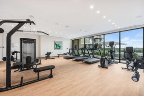 A modern gym with various exercise equipment, large windows, and a view of buildings outside. - StayShort - Stunning 2-Bedroom Apartment in Mina Rashid That Sleeps 6! (Dubai)