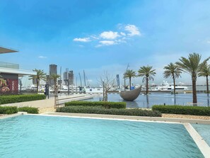 A swimming pool with a view of a marina and yachts, surrounded by palm trees and a modern building. - StayShort - Stunning 2-Bedroom Apartment in Mina Rashid That Sleeps 6! (Dubai)