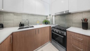 A modern kitchen with white cabinets, a stainless steel stove, and a tiled backsplash. - StayShort - Stunning 2-Bedroom Apartment in Mina Rashid That Sleeps 6! (Dubai)
