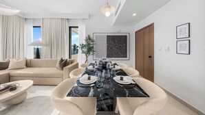 A modern living room with a dining area, featuring a marble table set for six, a sofa, and a large window with curtains. - StayShort - Stunning 2-Bedroom Apartment in Mina Rashid That Sleeps 6! (Dubai)