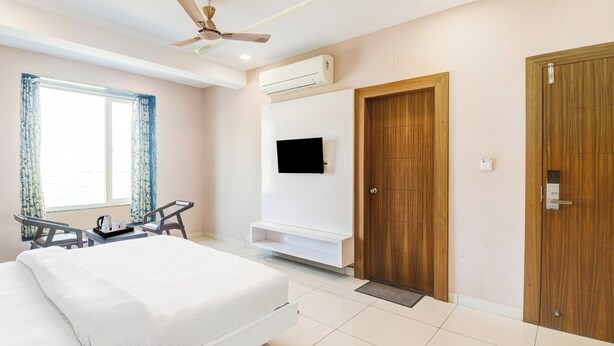 Habitación de hotel con cama, escritorio y silla, televisor montado en la pared y puerta de madera.