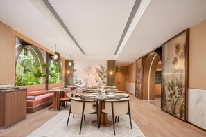 Un comedor moderno con mesas redondas, sillas y vistas a la vegetación a través de amplios ventanales.