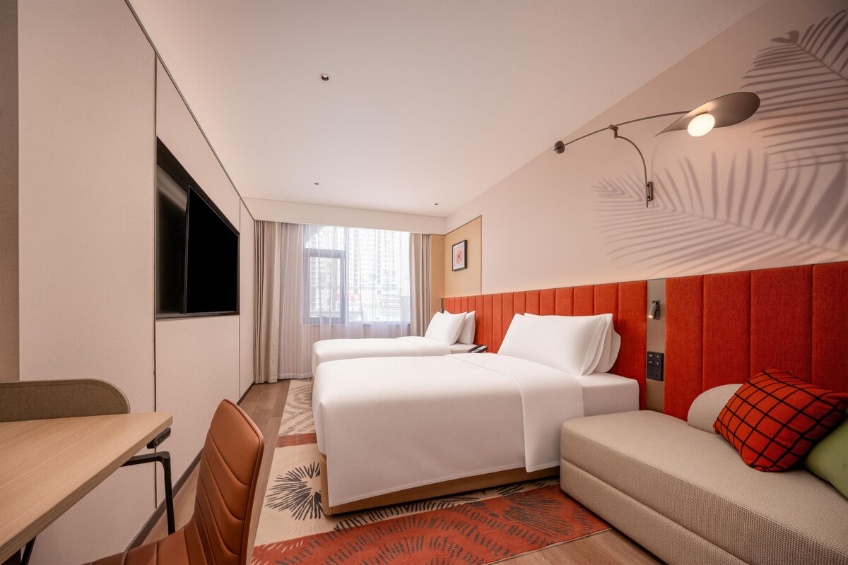 Ein Hotelzimmer mit zwei Betten, einem Schreibtisch und einem Fernseher.