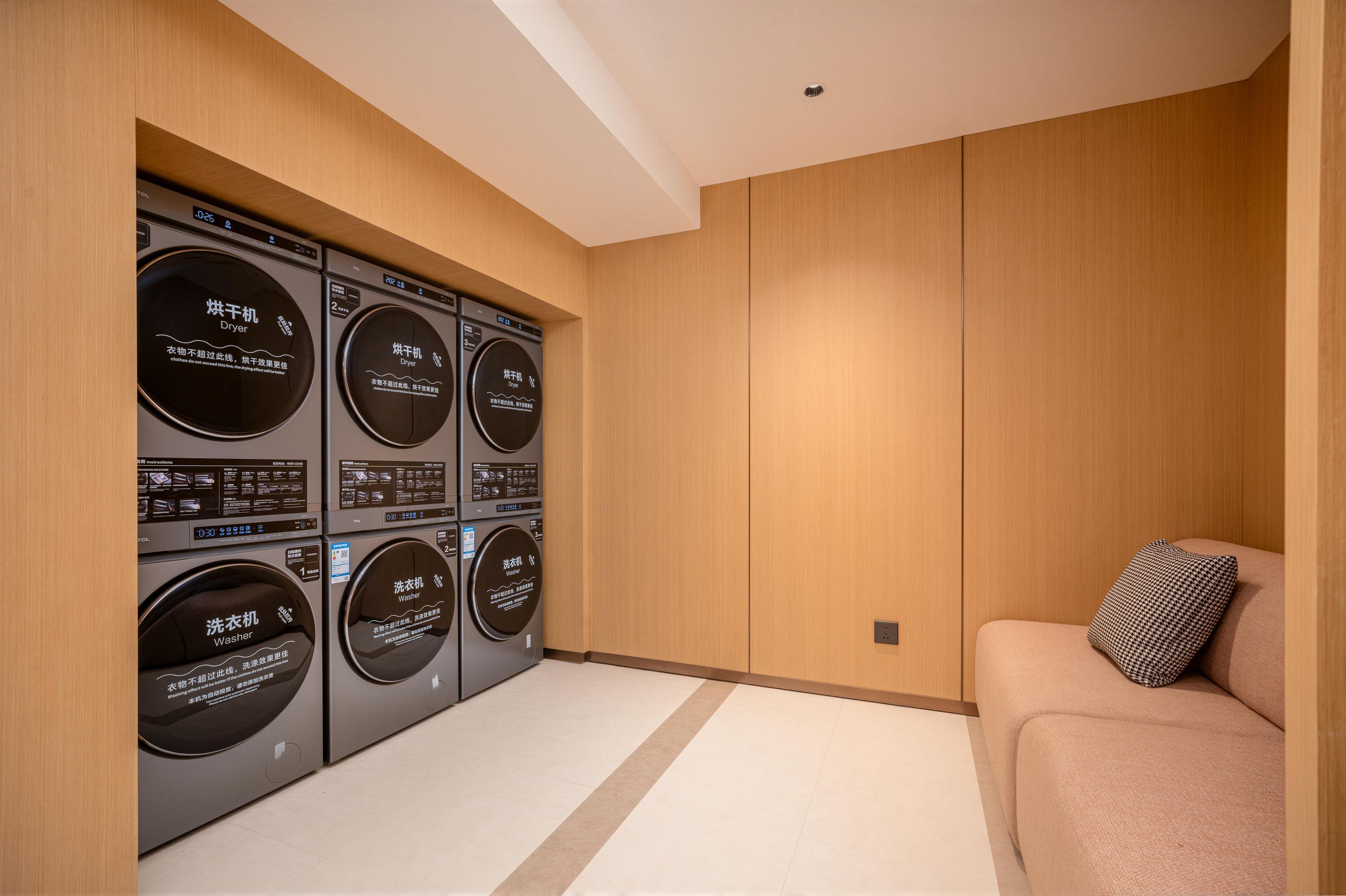 A laundry room with multiple washing machines and dryers, a beige sofa, and a wooden wall.