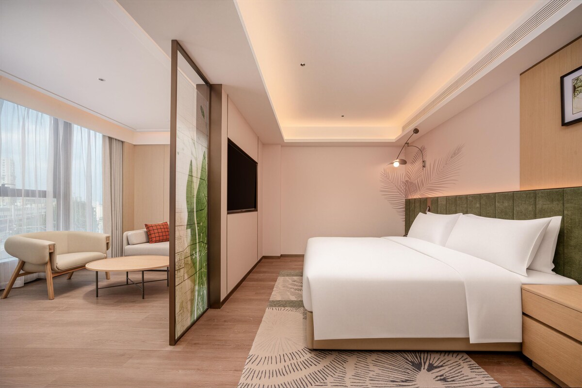 Ein modernes Hotelzimmer mit einem großen Bett, einer Couch, einem Schreibtisch und Blick auf die Stadt.