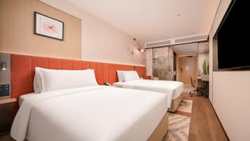 A hotel room with two beds, a desk, a television, and a bathroom visible through a glass door.