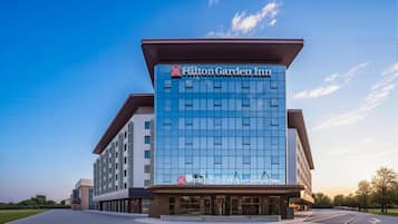 A modern hotel building with a prominent Hilton Garden Inn sign, featuring a glass facade and a flat roof.