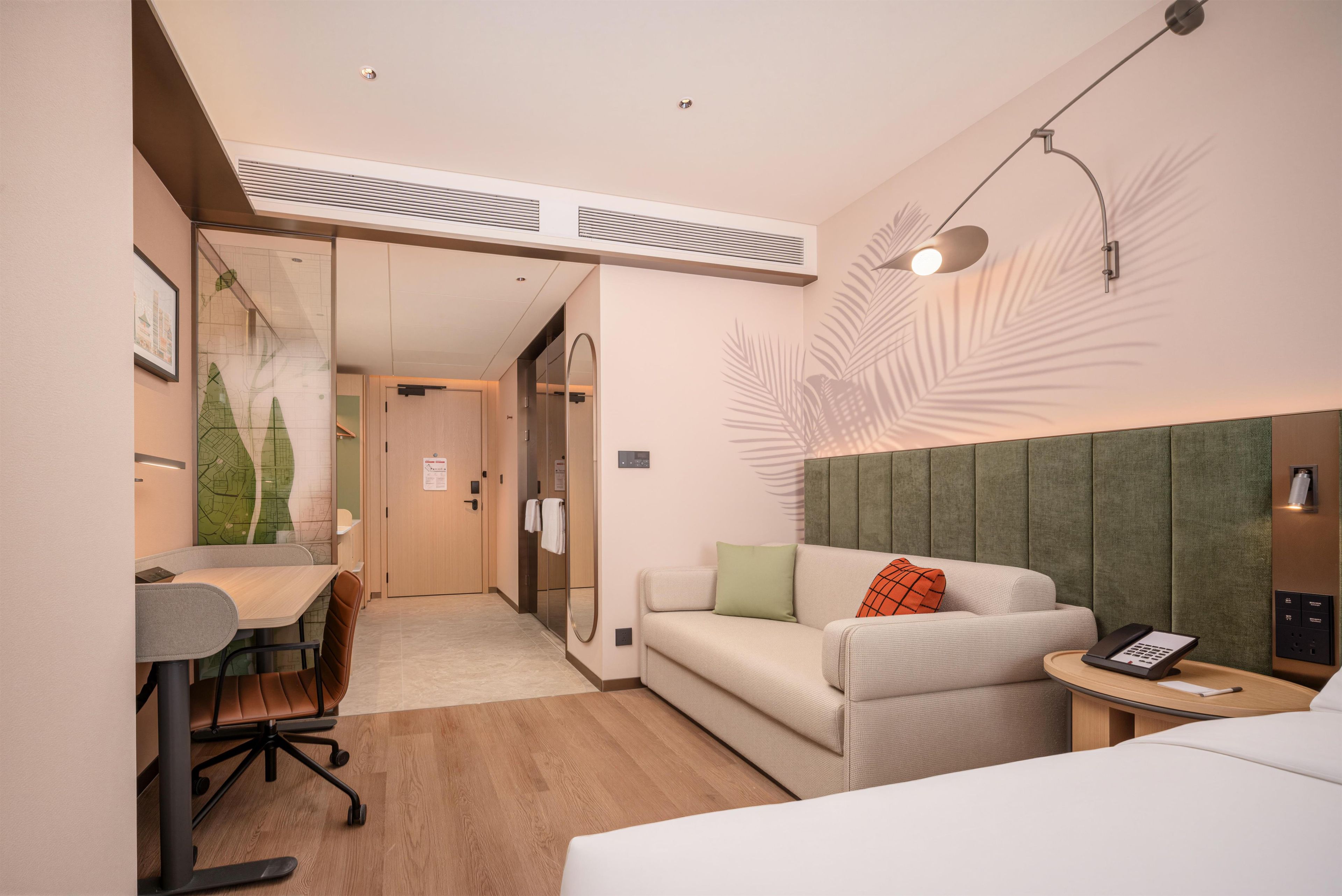 A hotel room with a bed, a desk, a chair, a sofa, and a small table with a phone.