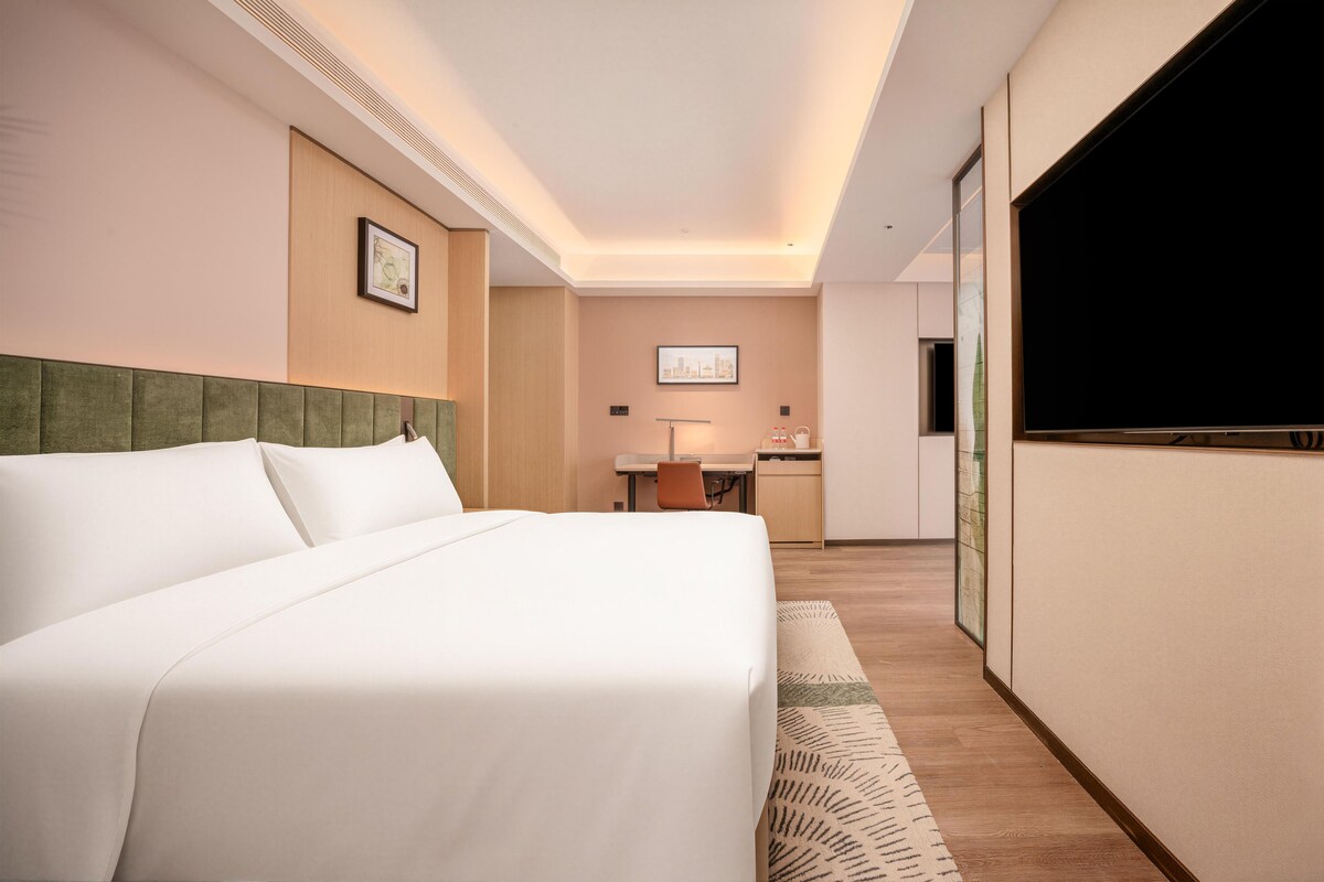 Habitación de hotel con una cama grande, un escritorio, una silla, un televisor de pantalla plana y un cuadro en la pared.