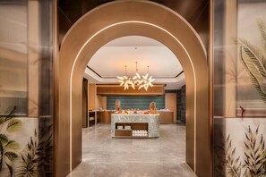 Um lobby moderno de hotel com uma recepção de mármore, um candelabro central e um balcão de madeira.