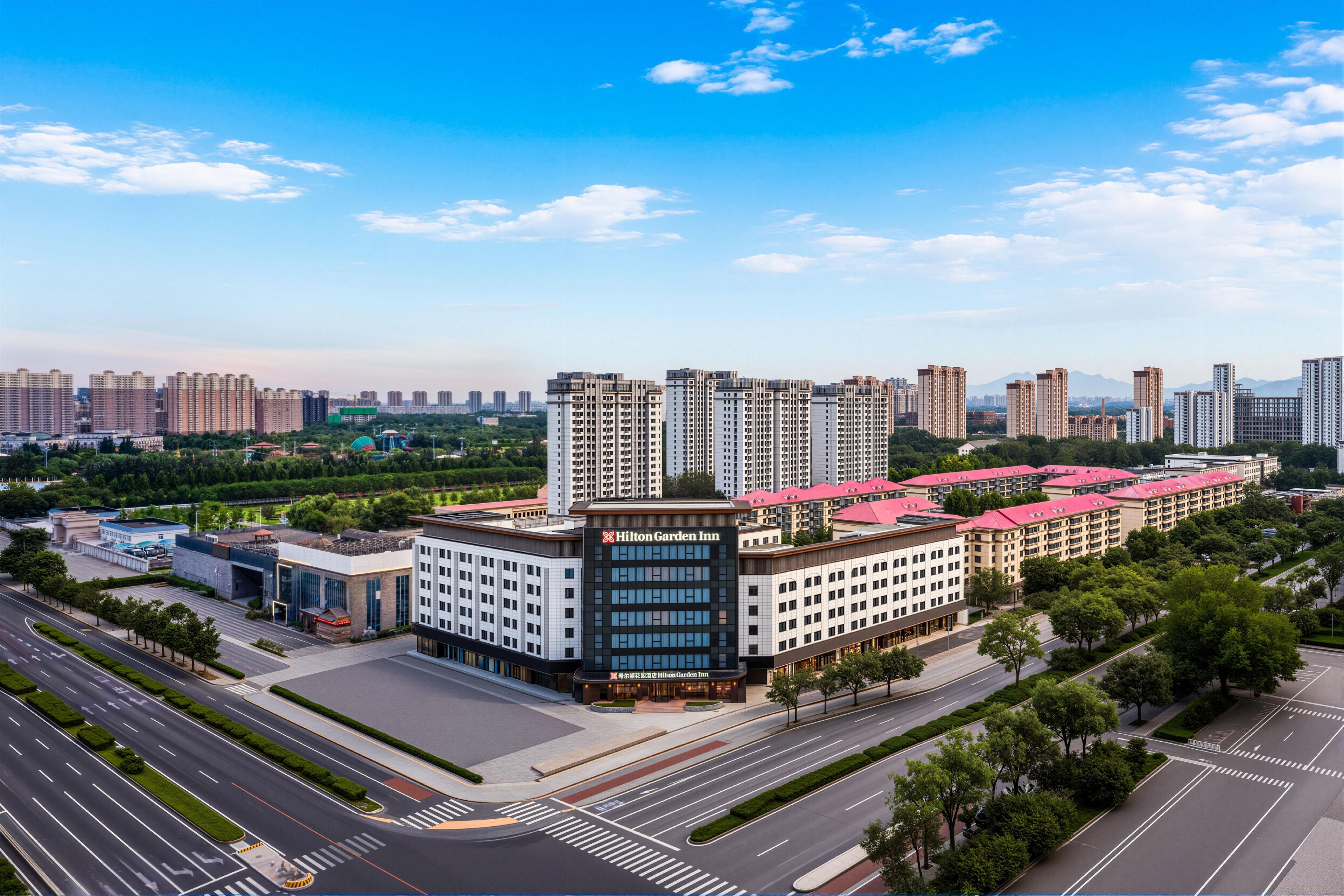 A multi-story hotel with a red roof, surrounded by a well-maintained urban environment with roads and greenery.