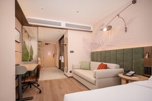 Quarto de hotel com cama, escrivaninha, cadeira, sofá e mesinha com telefone.