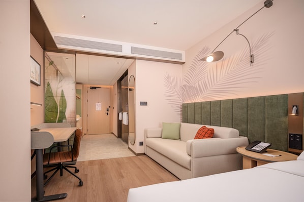 A hotel room with a bed, a desk, a chair, a sofa, and a small table with a phone.