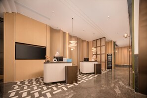Zona de recepción de un hotel con diseño moderno, que incluye un mostrador de recepción, una pantalla digital y una máquina expendedora.
