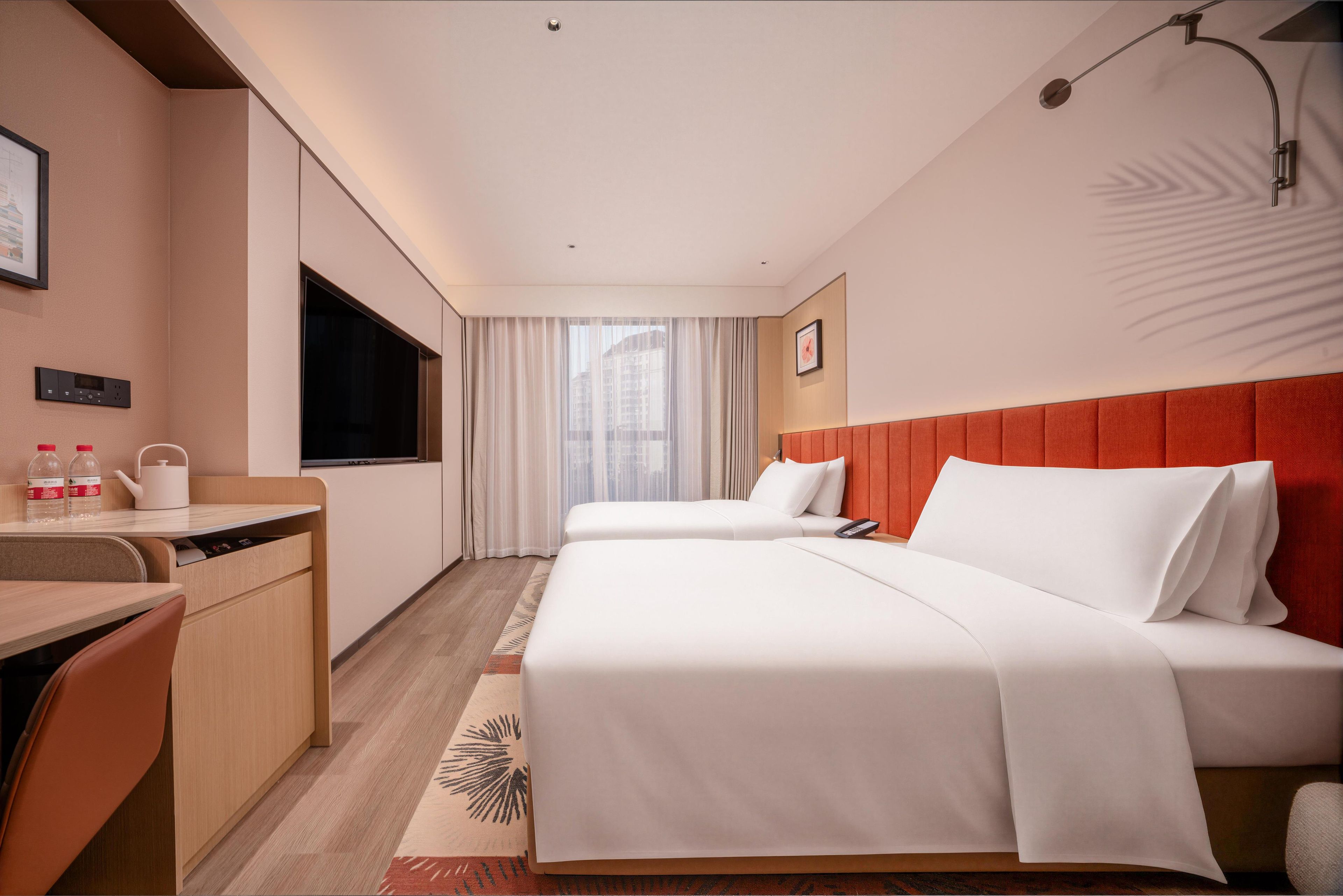 Una habitación de hotel con escritorio, dos camas, televisor y ventana con cortinas.