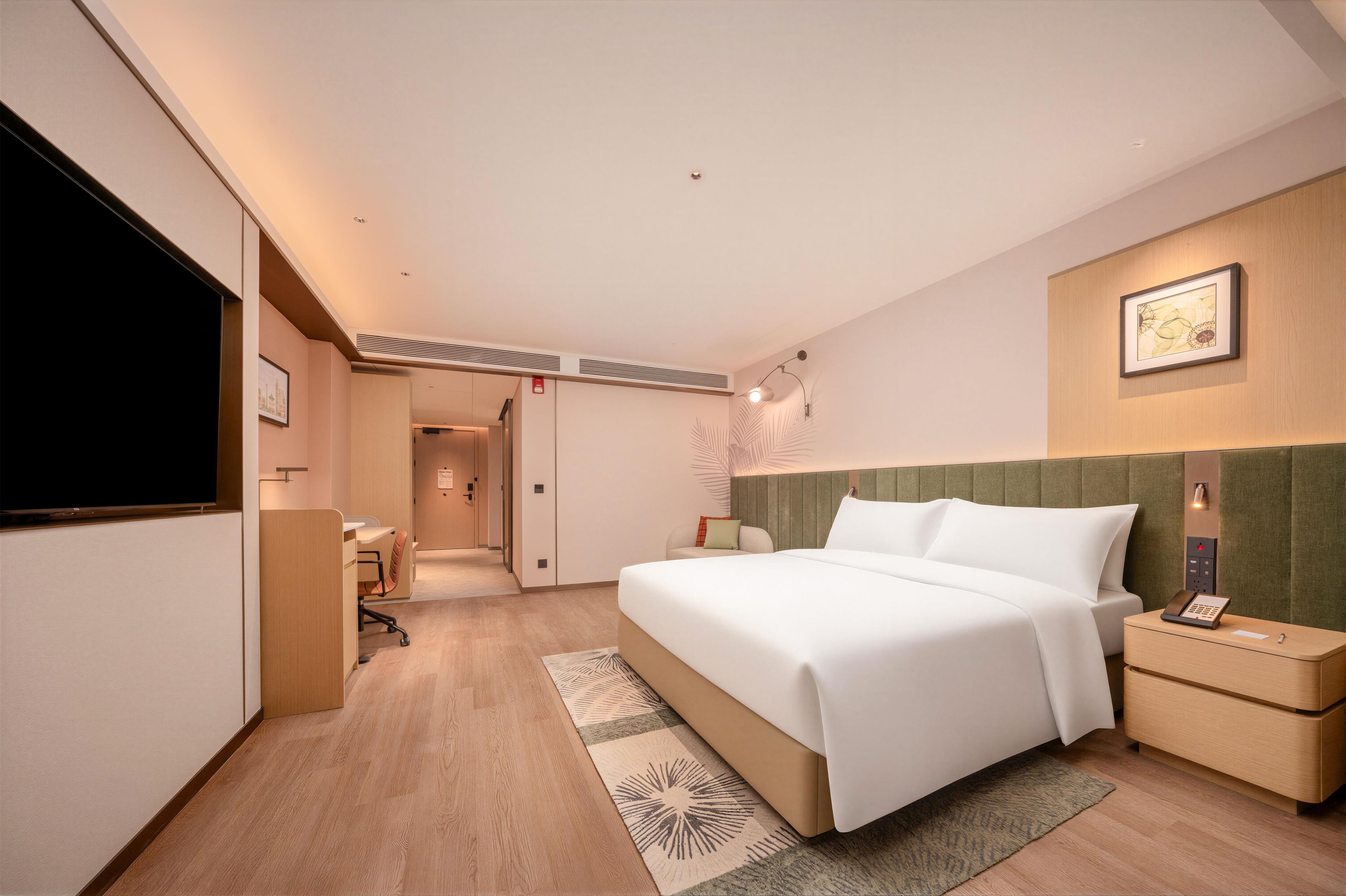 A hotel room with a bed, bedside table, and a desk with a chair.