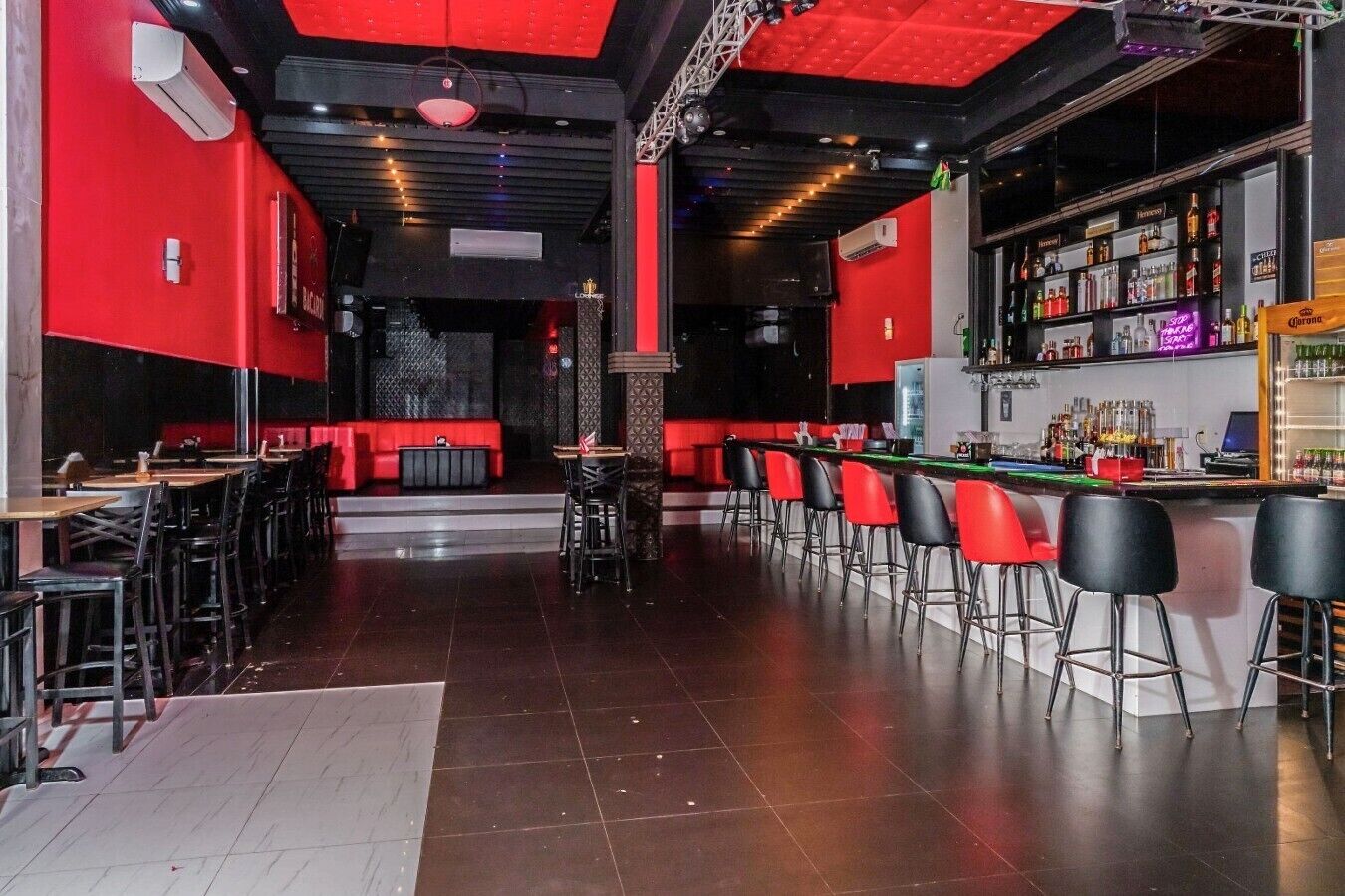 Un espace bar à la décoration rouge et noire, offrant différents types de sièges et une grande variété de bouteilles exposées sur des étagères.