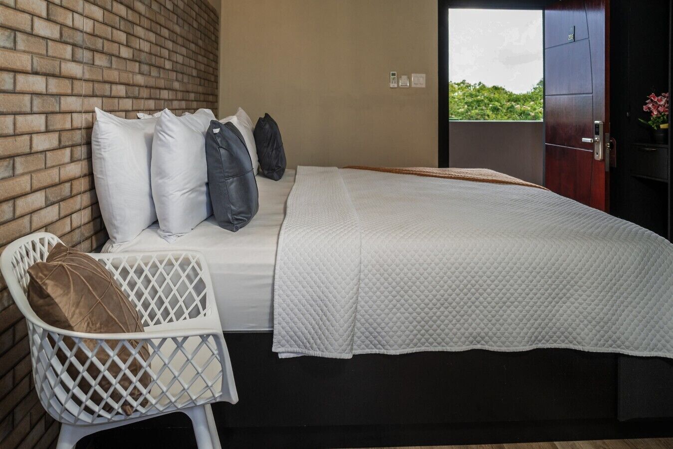 A bedroom with a bed, pillows, a white chair, and a view through an open door.