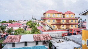 A multi-story building with balconies, a red roof, and a view of surrounding buildings and greenery.