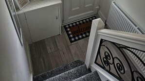 A white front door with a small window, a welcome mat, and a staircase leading to an upper floor. - Home -near Town/lutonairport Sleeps 6/parking/wifi (Luton)