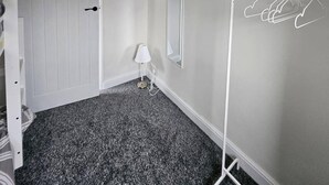 A room with a white door, a small table with a lamp, a coat rack, and a carpeted floor. - Home -near Town/lutonairport Sleeps 6/parking/wifi (Luton)