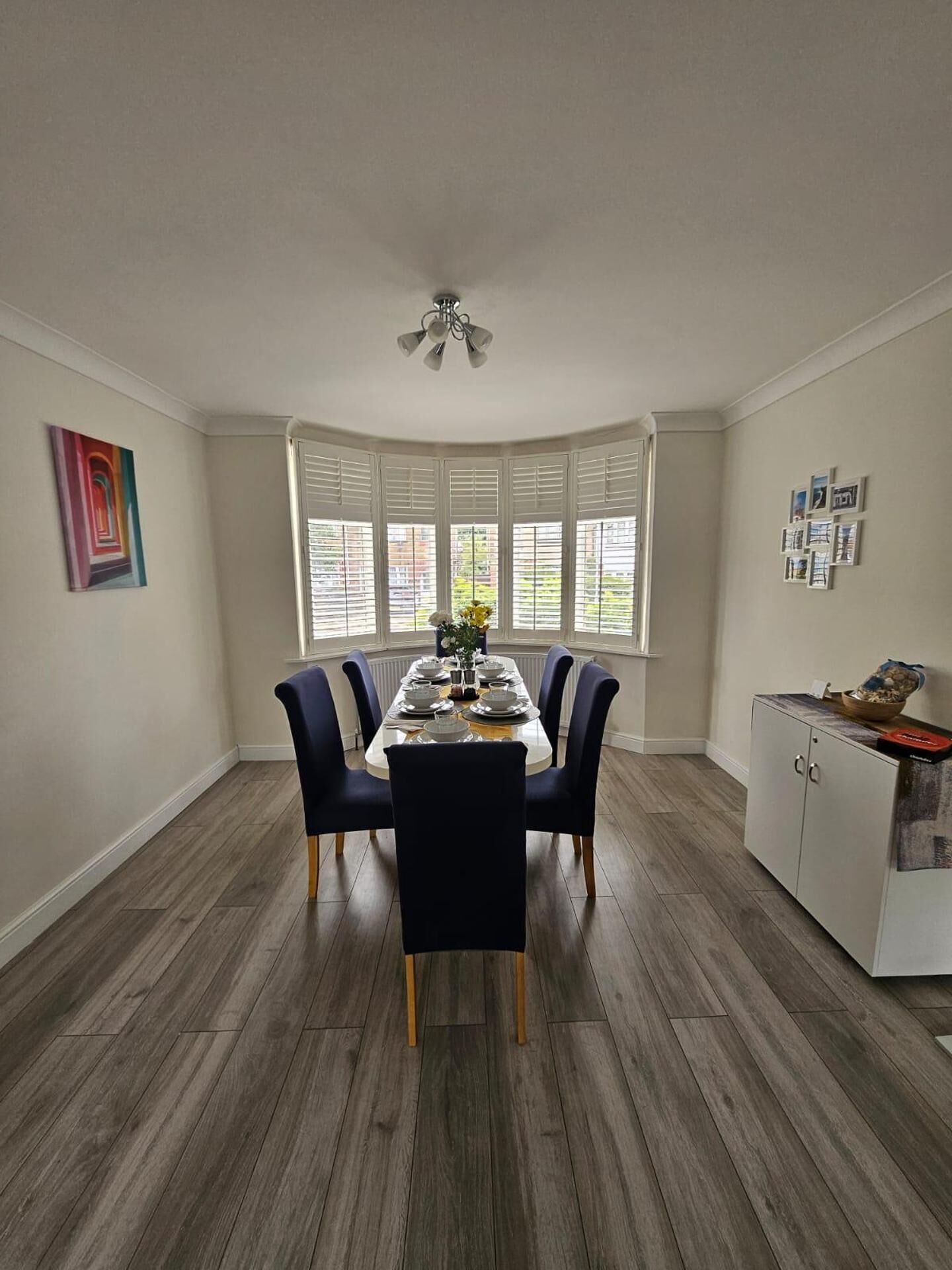 A dining room with a bay window, a white cabinet, and a ceiling fan.
