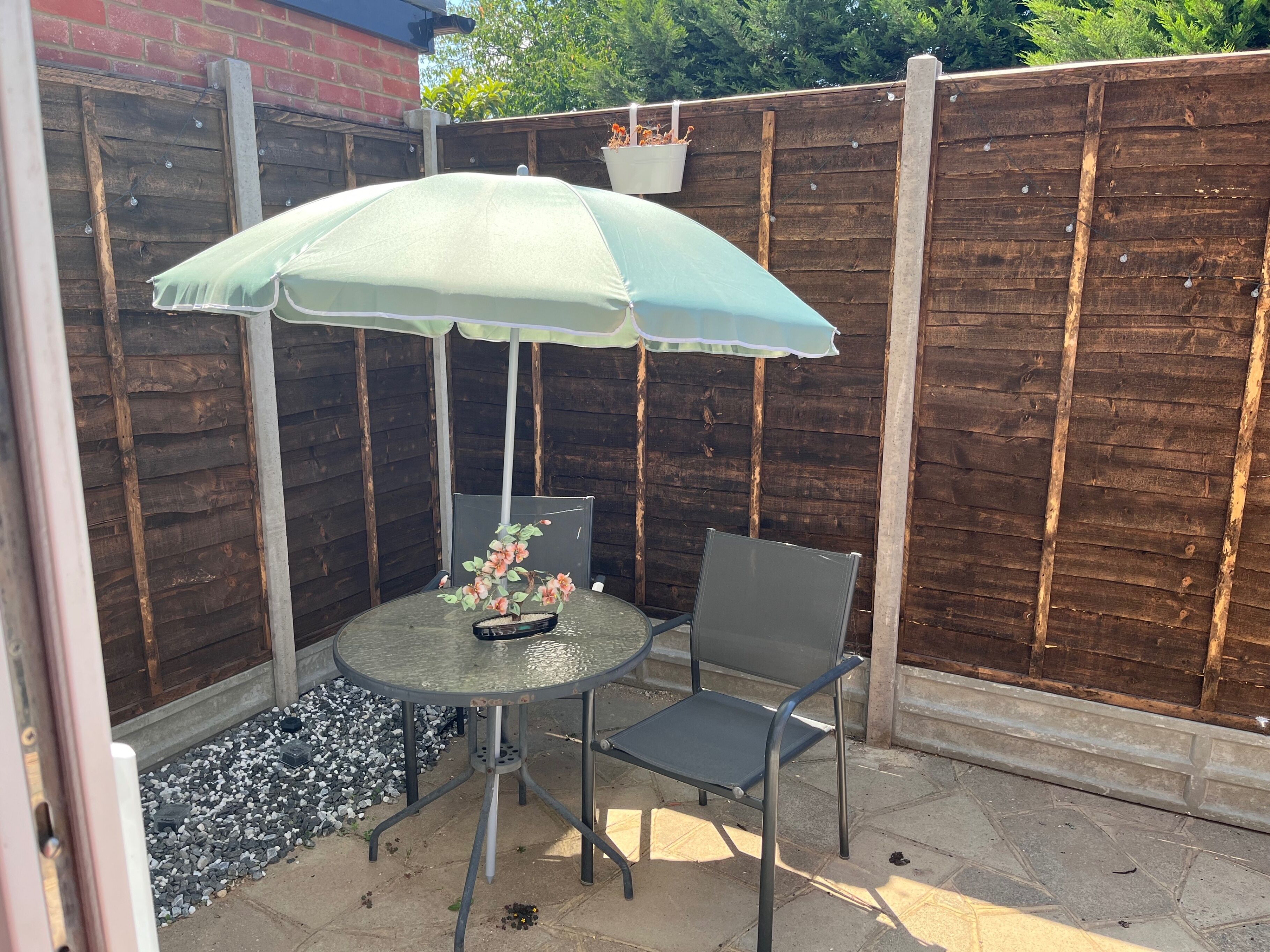 Une terrasse avec une table et des chaises, un parasol et un pot de fleurs suspendu.