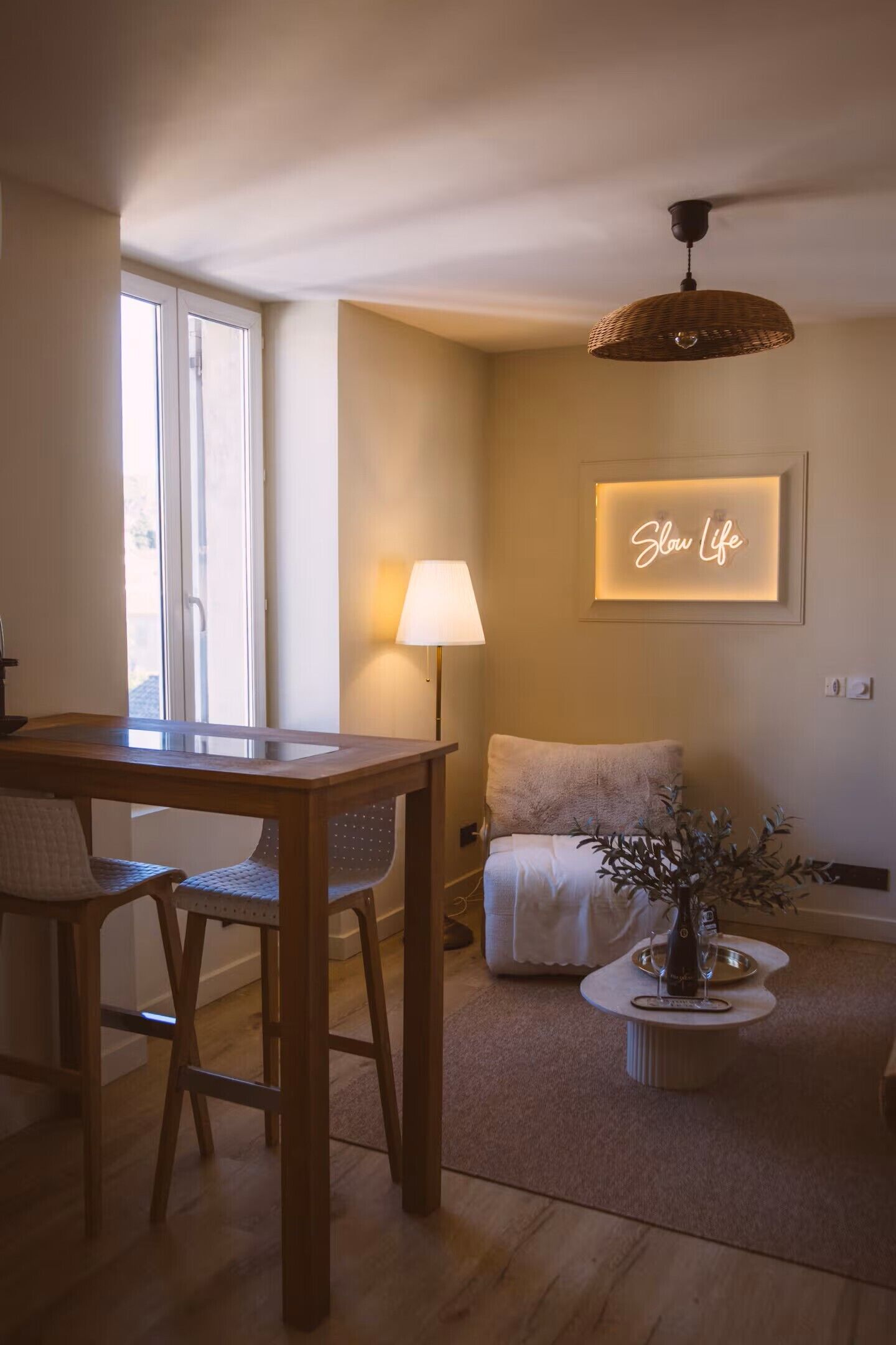 A modern living room with a dining area, a ceiling fan, a lamp, a wall-mounted sign, and a small table with a vase.